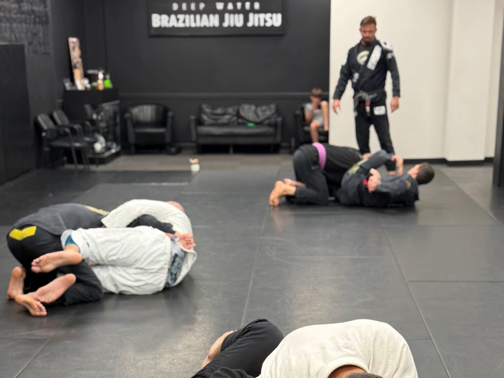 Brazilian Jiu-Jitsu students practicing in pairs during a coached class at Deep Water BJJ.